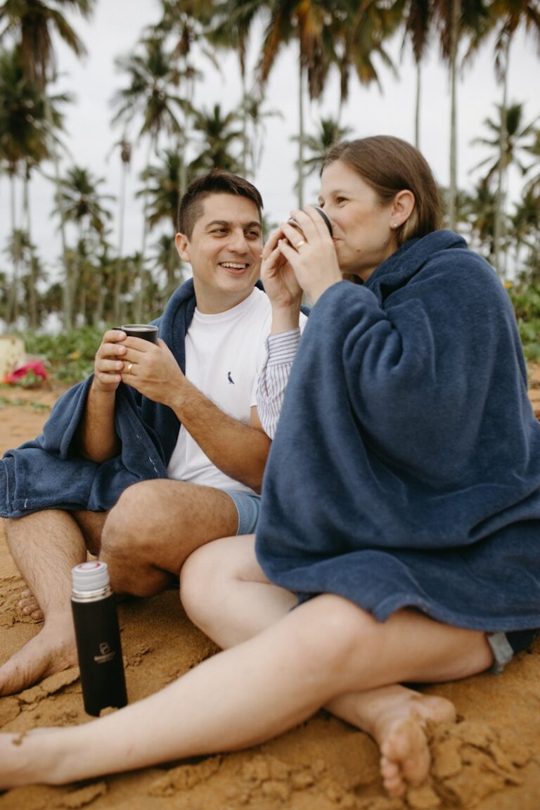 Engaged couple relaxing together on a beach, representing mental wellness during wedding planning