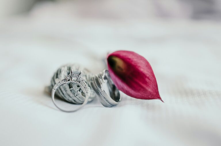 Close-up of a custom silver wedding ring with intricate design beside a pink flower