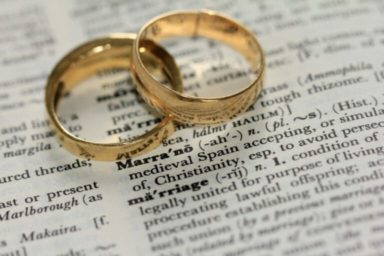 Two gold wedding bands placed on a dictionary page, symbolizing wedding ring care and meaning